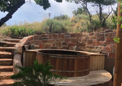 a single wall hot tub set in a deck with stone stairs and stone wall behind it.