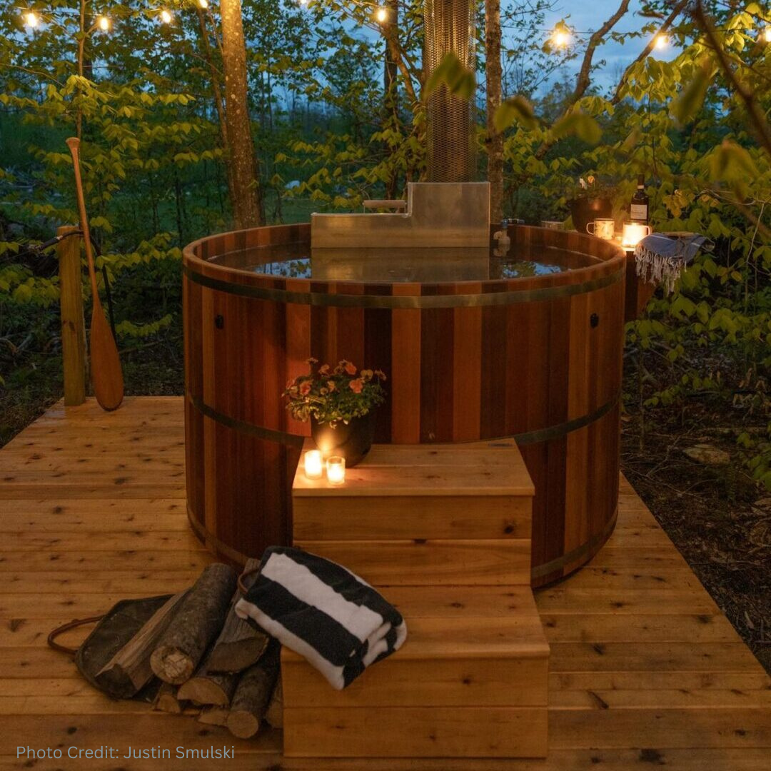 Cedar wood-fired hot tub surrounded by the woods in a romantic setting with candles.